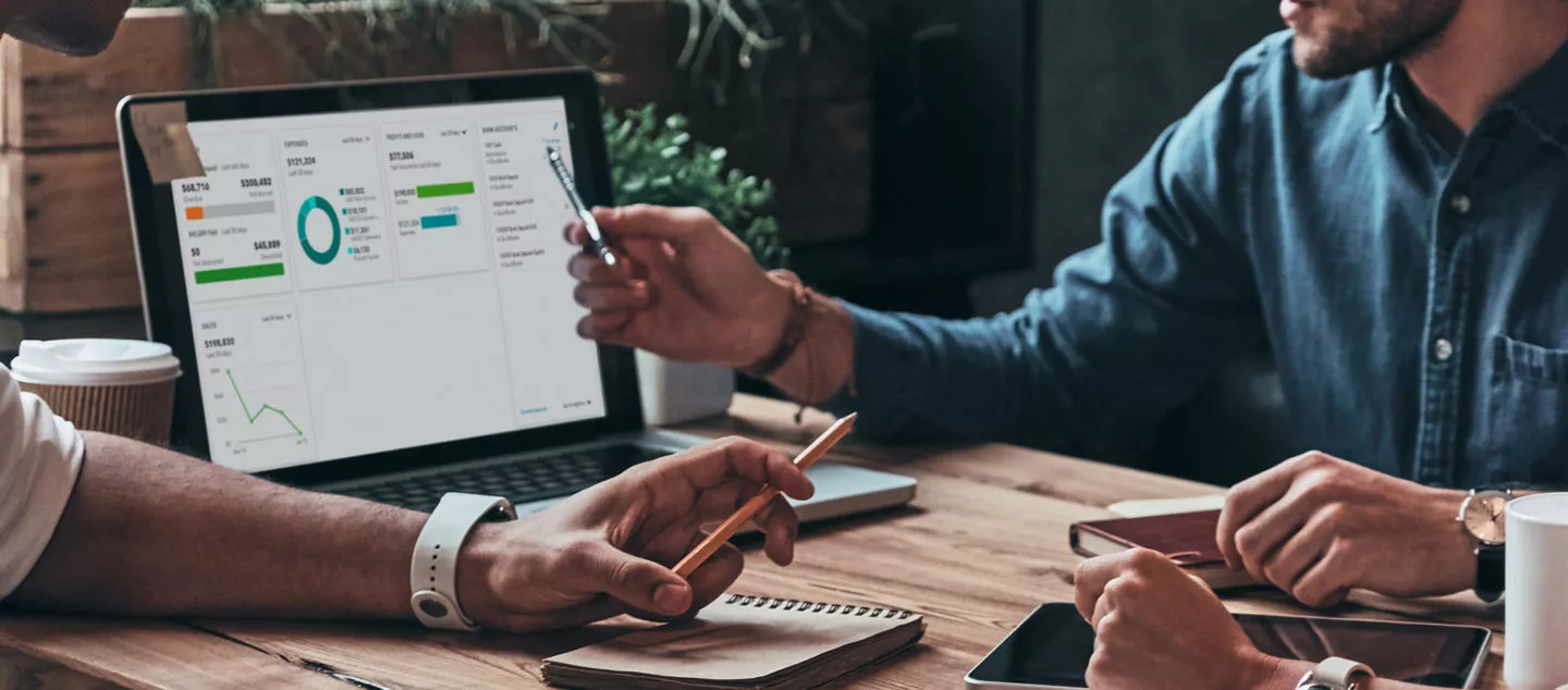 Two people sitting at table analyzing financial reporting on a laptop.