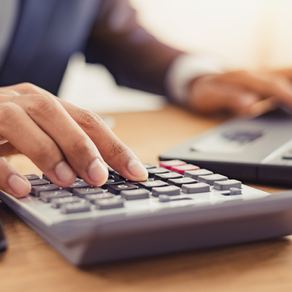 Businessman with one hand typing on a calculator and the other typing on a laptop to process payroll.
