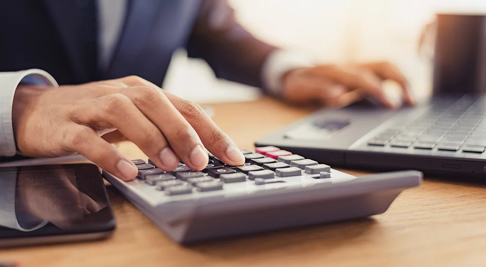 Close up of man's hands using calculator and laptop.