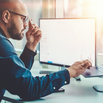 Man looking at computer while the sun streams in the window.