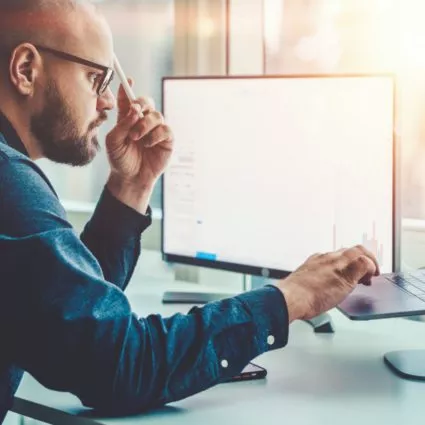 Man looking at computer while the sun streams in the window.