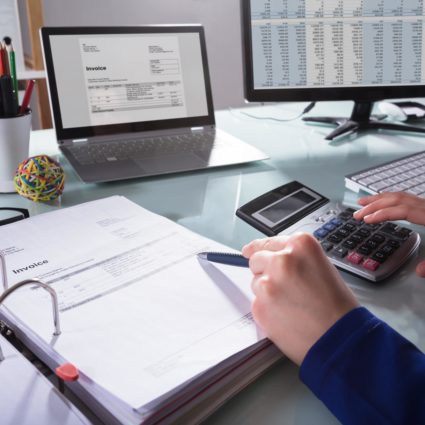 A person working at their desk with a computer, calculator, and paperwork on it.