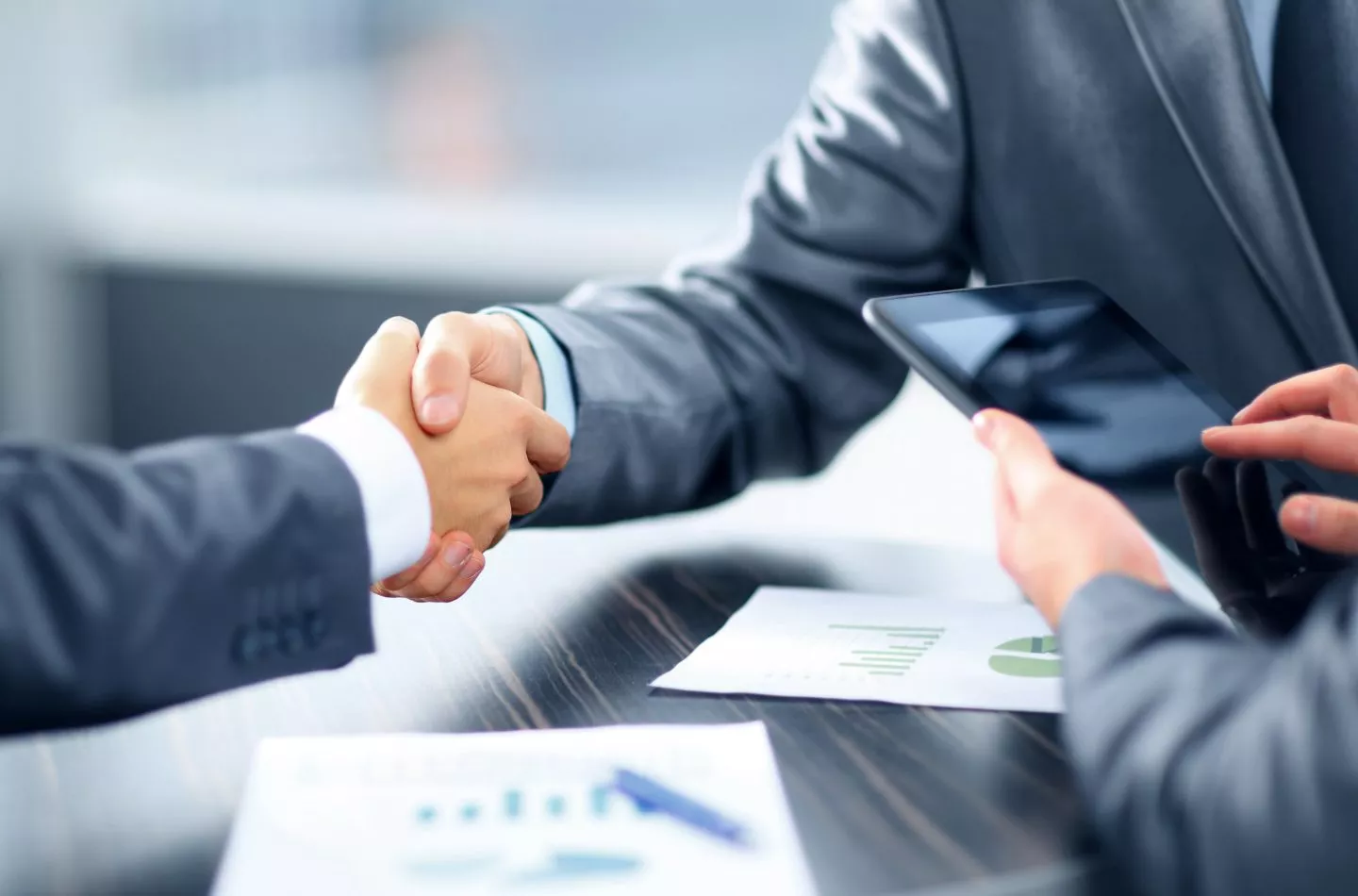 Two men shaking hands with financial documents on the desk