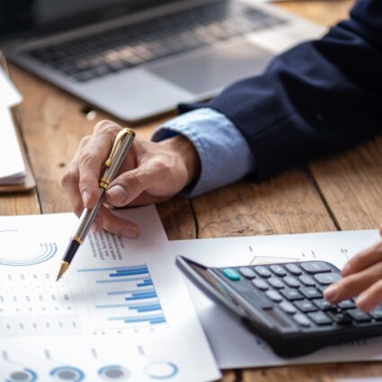 A man working on a calculator while referencing some financial reports with graphs